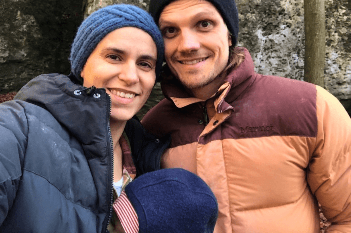Klettern mit Baby outdoor: Familie müde aber glücklich mit Baby in der Trage am Wandfuß eines Klettergebiets