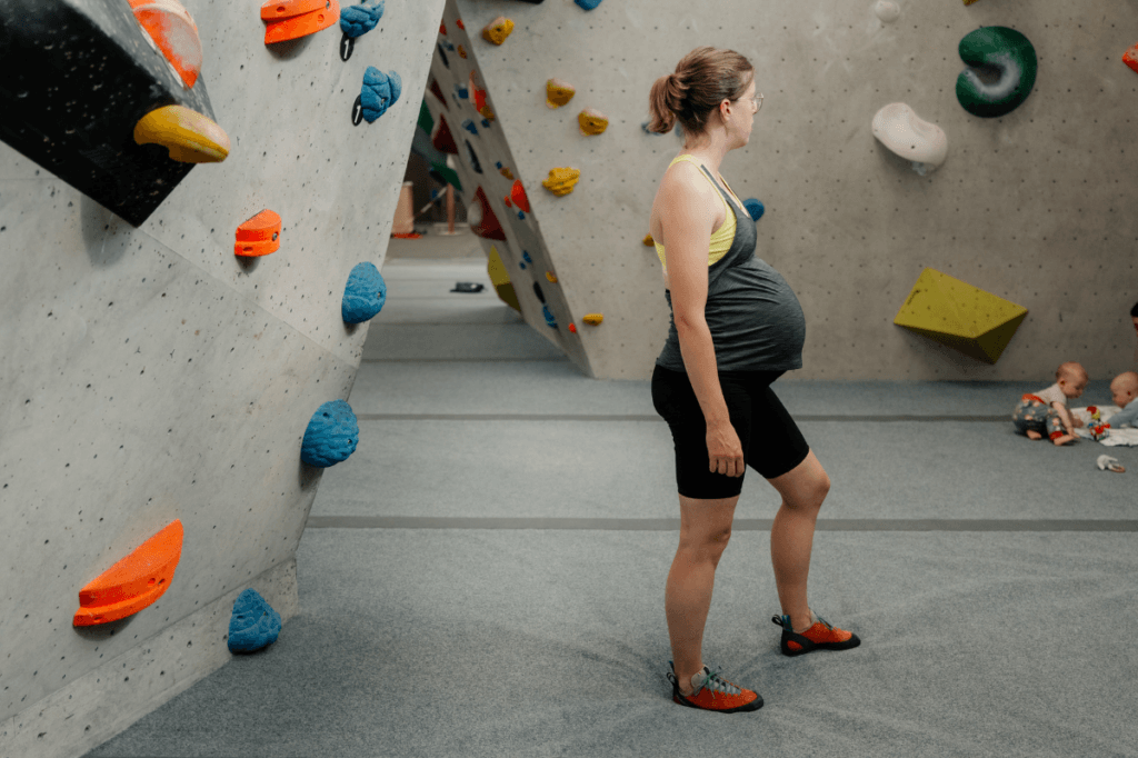 Bouldern in der Schwangerschaft: Schwangere Kletterin steht in der Boulderhalle und schätzt ab, ob sie einsteigt oder heute aussetzt