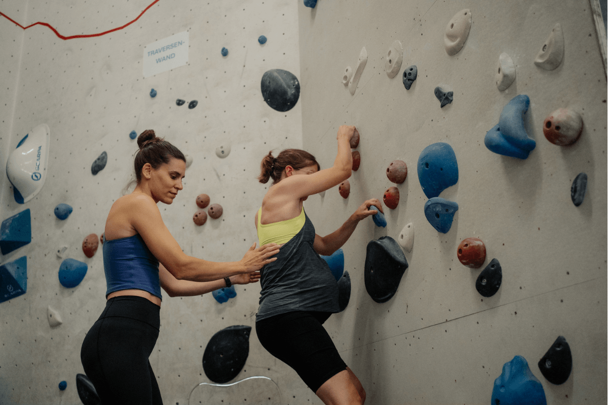 Bouldern in der Schwangerschaft: Schwangere Kletterin klettert kontrolliert bodennah, ihr Spotter steht dicht hinter ihr